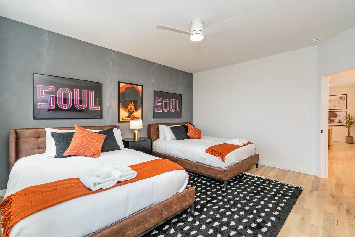 A vibrant bedroom with two large beds adorned with bright bedding, energetic soul-themed artwork above the beds, and colorful wall art. The room exudes creativity and flexibility for friends or families sharing the space.