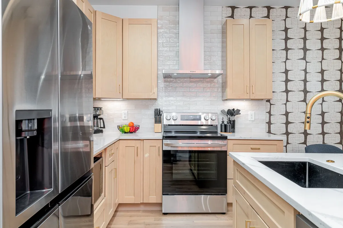 A modern kitchen with stainless steel appliances, a white subway tile backsplash, wood cabinetry, and a contemporary light fixture. The layout is open and inviting, suitable for both cooking and family gatherings.