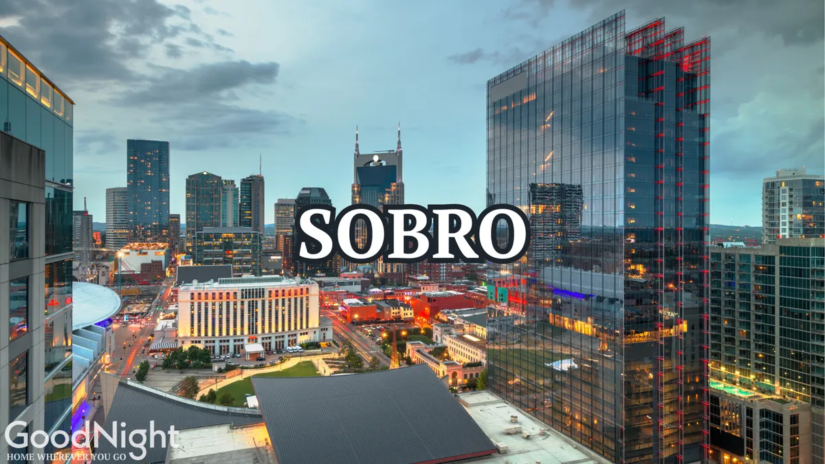 A stunning cityscape view at dusk, featuring Nashville's skyline lit up with colorful lights and the prominent 'SOBRO' sign. The image evokes a sense of adventure, urban excitement, and the allure of exploring vibrant neighborhoods after dark.