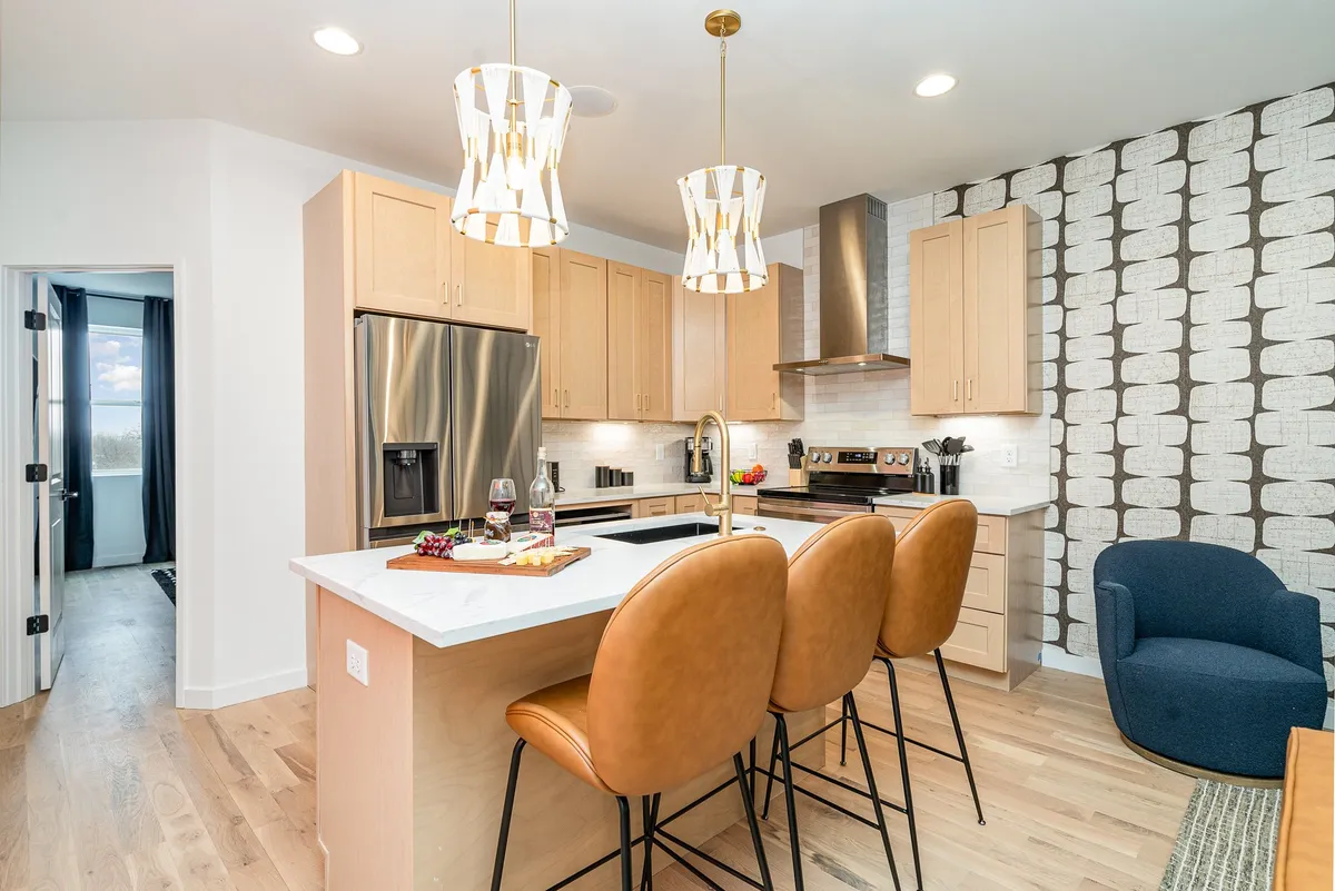 A contemporary kitchen space with inviting island seating, sleek modern appliances, and eye-catching light fixtures. The textured wall adds warmth, while the ample island and seating encourage group interaction and casual breakfasts.
