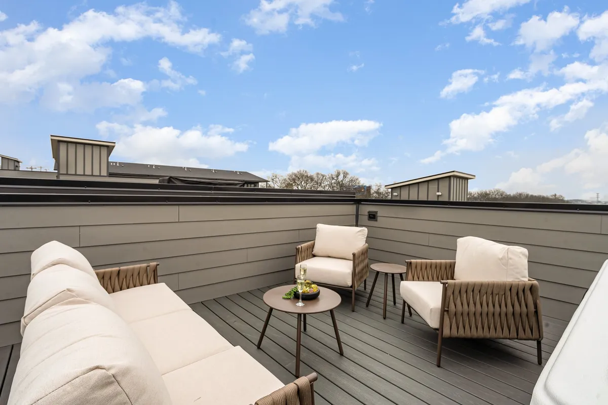 A cozy outdoor seating area with a small table and comfortable chairs, positioned to take in open sky views. The space feels tranquil, ideal for relaxing with a drink as city lights begin to twinkle.